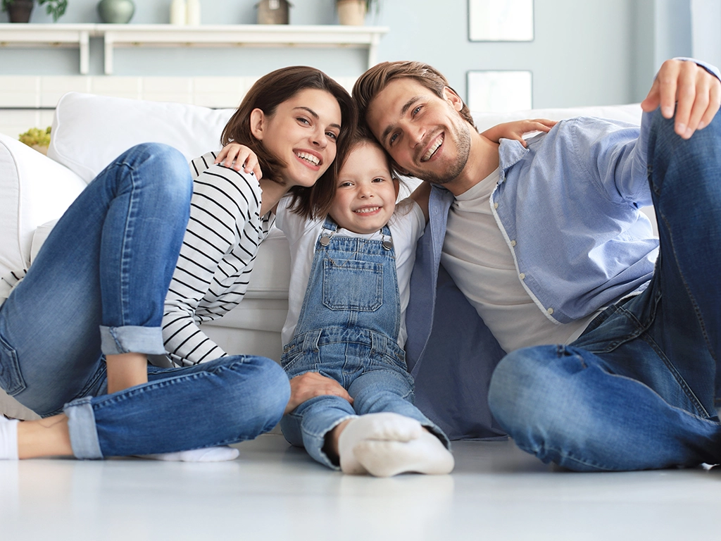 young family with small daughter relaxing and smiling on livingroom floor